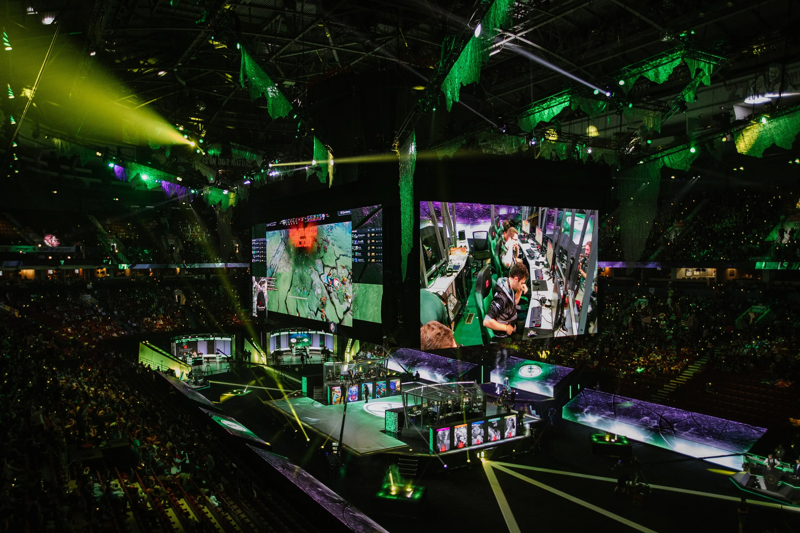 Arena de esports iluminada en verde con pantallas y público alrededor del escenario.